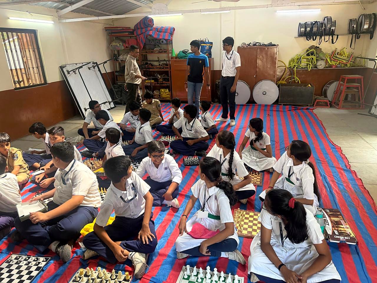 Students in school uniforms seated beside chessboards in a classroom.